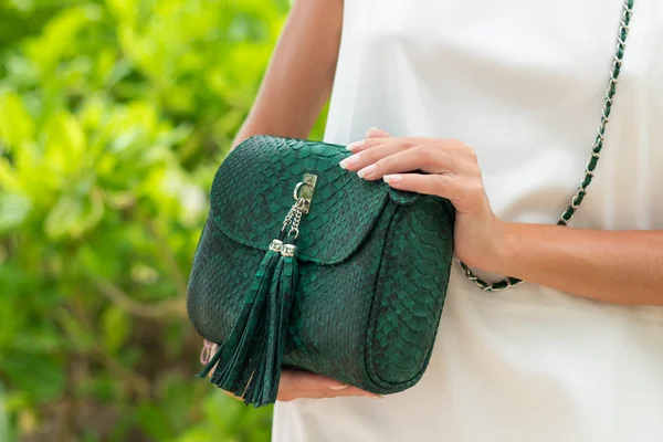 Woman hands with luxury handmade green snakeskin python handbag. Beautiful asian background.