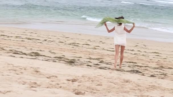 Τρέχει γυναίκα παραλία σε εξωτερικούς χώρους. Νεαρή όμορφη γυναίκα με γυαλιά και πράσινο μετάξι κασκόλ, Μπαλί, Ινδονησία. — Αρχείο Βίντεο