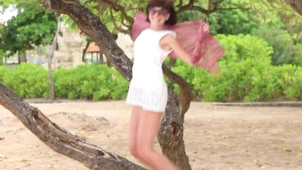 Повільний рух сексуальна жінка стрибки на пляжі, кружляння з Шовковий шарф. Красиве тло з пальмами та інші азіатські рослини. Балі, Індонезія. — стокове відео