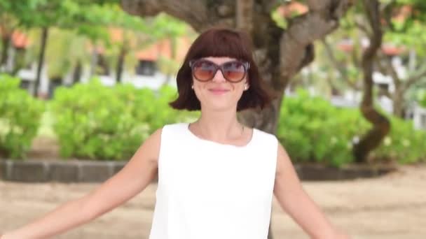 Mujer joven feliz en vestido blanco con gafas de sol y bufanda de seda balinesa girando en la playa. En cámara lenta. Bali, Indonesia . — Vídeos de Stock