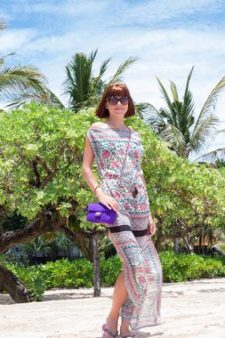 Sahilde poz beyaz elbiseli esmer manken. Güneş gözlüğü ve lüks handmande yılan derisi python el çantası giyiyor. Bali, Endonezya.