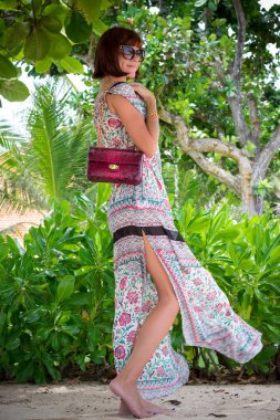 Sahilde poz esmer manken. Güneş gözlüğü ve lüks handmande yılan derisi python el çantası giyiyor. Bali, Endonezya.