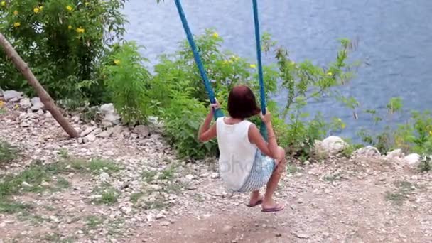 Ung flicka gungar på en gunga i bergen på en klippa ovanför havet. Fantastisk utsikt, slowmotion. Tropiska ön Ceningan, Indonesien. — Stockvideo