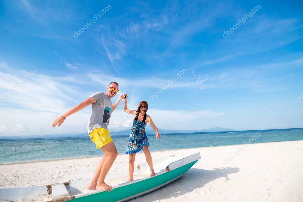 Happy young joyful couple having beach fun laughing together during summer holidays vacation on tropical beach with white sand. Beautiful energetic fresh interracial multi-ethnic couple, man and woman