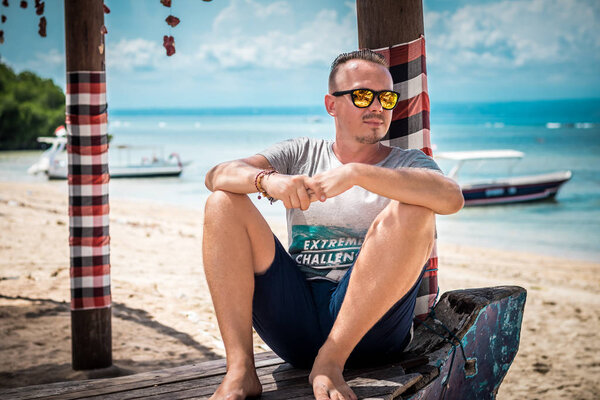 Портрет привлекательного молодого кавказца в солнечных очках, позирующего на тропическом пляже Нуса-Лембонган, Индонезия. Солнечный день летом
.