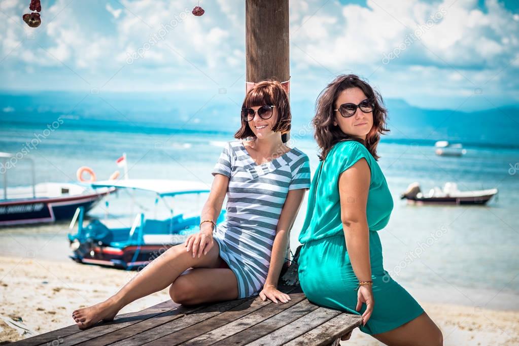 Summer vacation, holidays, travel, friendship and people concept - two smiling young women on the beach of tropical island Nusa Lembongan, Indonesia, Asia. Sunny day, beautiful background. HDR photo.