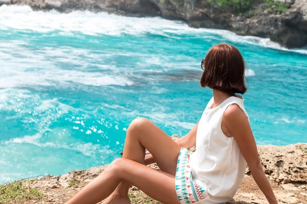 Libertad joven mujer caucásica sentado y posando en la roca pico de la montaña, acantilado. Hermoso océano azul en el fondo. Isla tropical Nusa Lembongan, Bali, Indonesia, Asia. Concepto de verano . — Foto de Stock