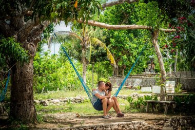 Mutlu bir genç Romantik Çift birlikte bir hamakta tropikal üzerinde onların tatil sırasında oturmak istiyor portresi ada Bali, Endonezya. Aşk sahnesi. Asya.