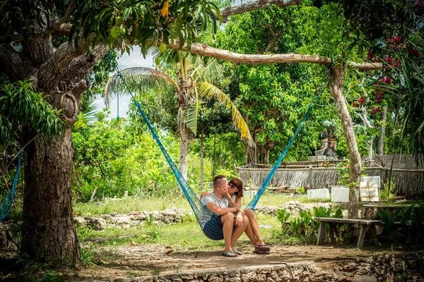 Retrato de una feliz pareja romántica joven tratando de sentarse juntos en una hamaca durante sus vacaciones en la isla tropical de Bali, Indonesia. Escena de amor. Países Bajos . — Foto de Stock
