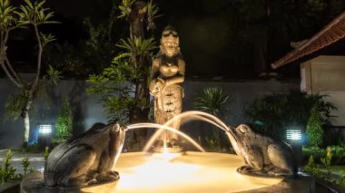 Zaman atlamalı küçük sihirli Bahçe Çeşmesi. Gece sahne. Su sürahi kadın elinde, kurbağalar gelir. Asya çeşme. Bali, Endonezya.