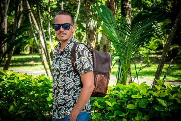 Touristique avec élégant sac à dos python en peau de serpent brun dans le parc asiatique. Bali, Indonésie. bel homme caucasien dans les lunettes de soleil . — Photo
