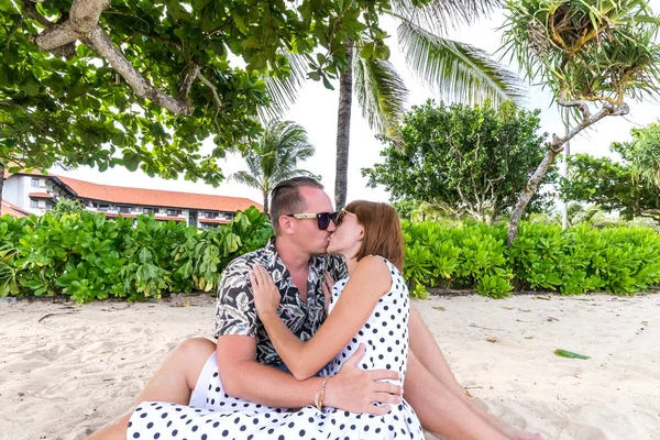 幸せなロマンチックな新婚旅行のビーチの砂の上に座っているカップルします。背景にヤシの木.バリ島、インドネシア. — ストック写真