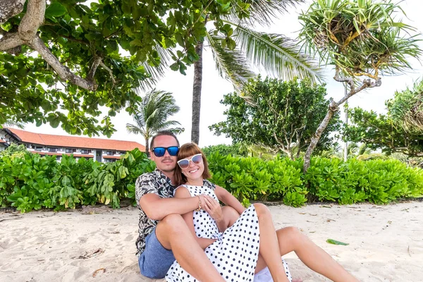 Feliz casal de lua-de-mel romântico na praia sentado na areia. Palmas em um contexto. Bali Island, Indonésia . — Fotografia de Stock