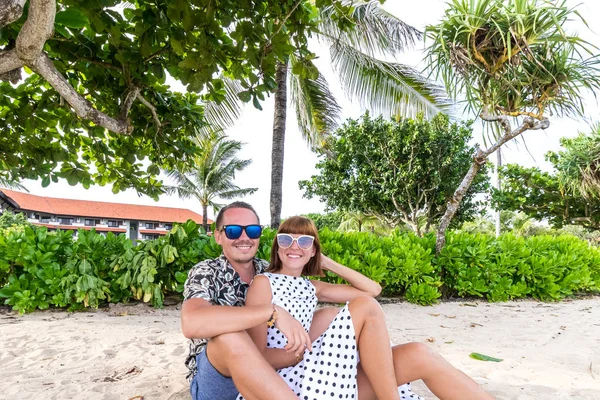 Feliz casal de lua-de-mel romântico na praia sentado na areia. Palmas em um contexto. Bali Island, Indonésia . — Fotografia de Stock