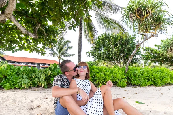 Felice coppia romantica luna di miele sulla spiaggia seduta sulla sabbia. Palme su uno sfondo. Isola di Bali, Indonesia . — Foto Stock