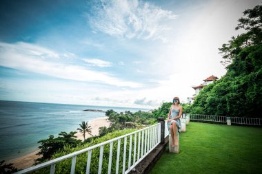 Bir yaz gününde Okyanusu yakınlarındaki mavi gözlüklü genç çekici beyaz kadın. Yeşil ile mavinin muhteşem sahne. Tropik ada Bali, Endonezya, Asya.