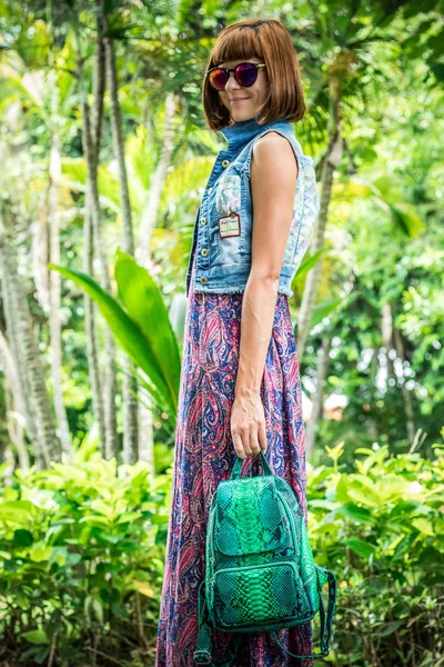 Elegant lady with stylish short hairstyle and glasses holding a luxury snake skin python backpack. Bali island. Asia, Indonesia.