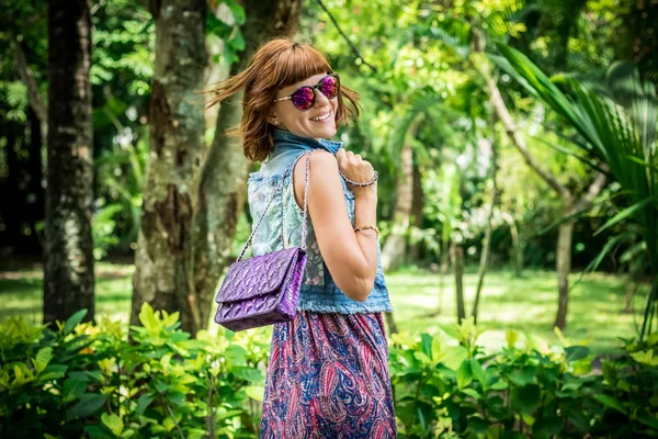 美丽时尚白种人黑发女人带着墨镜摆在公园的努沙杜阿，印度尼西亚巴厘岛的豪华蛇皮 python 手提包的画像。亚洲。阳光灿烂的日子，绿色背景. — 图库照片