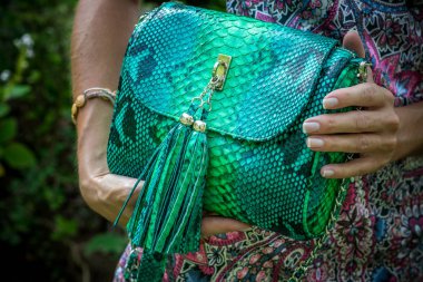 Young woman holding a luxury handmade snakeskin python handbag. Sunny day. Expensive clutch. Close up of woman hands with bag.