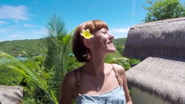 Mutlu kadın turist üzerinde bir tropik ada Nusa Lembongan, Bali, Endonezya. Kız Gezgin neşeli ve mutlu gülümseyerek çevresinde arıyorum. Plumeria frangipani çiçek onun kulağına.
