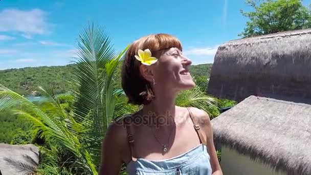 Щасливі жінка туриста на справжній тропічний острів Нуса Лембонган, Балі, Індонезія. Дівчинка мандрівник озираючись радісне і щасливі посміхаючись. Квітка frangipani Живці квітів у її вухо. — стокове відео