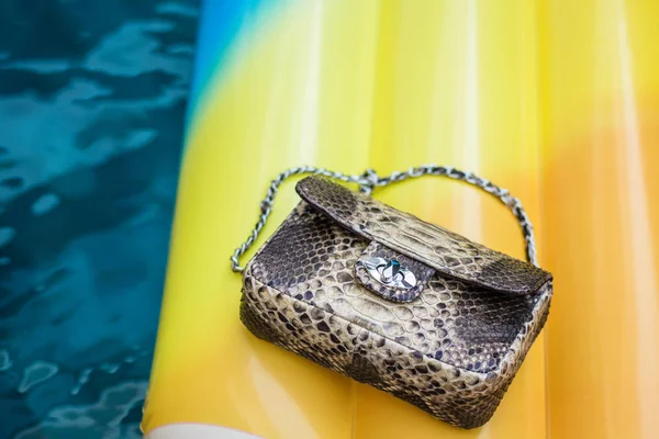 Fashion luxe slangenhuid python handtas op een opblaasbare gele matras in zwembad. Zomer stemming. — Stockfoto
