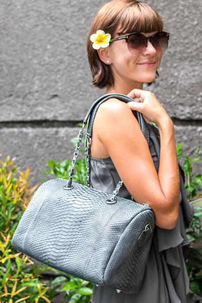 Fashionable woman holding luxury stylish snakeskin python bag. Elegant outfit. Close up of purse in hands of stylish lady. Model posing. Female fashion.