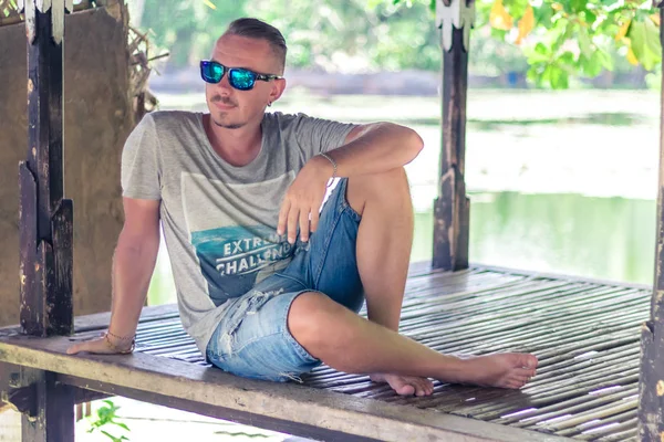 Handsome man enjoying his summer holidays outdoors the tropical Bali island, Indonesia. Portrait of young man in wooden gazebo. — Stock Photo, Image