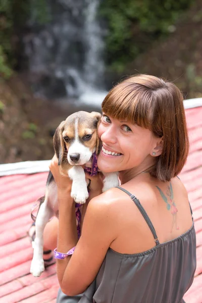 Pretty woman beautiful young happy with small dog puppy beagle. Tropical island Bali, Indonesia. Lady with beagle, waterfall on a background. Love scene.