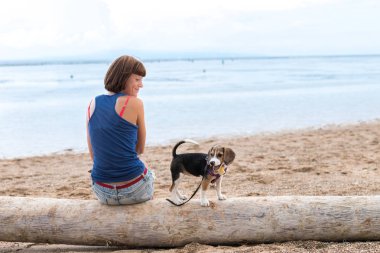 A beagle köpek köpek yavrusu ile sahilde oturan güzel kız. Tropik ada Bali, Endonezya.