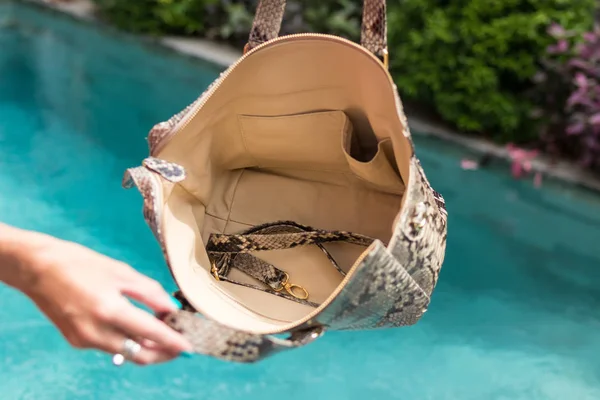Close-up van de hand van de vrouw die mode slangenhuid python tas in de buurt van het tropische zwembad. — Stockfoto