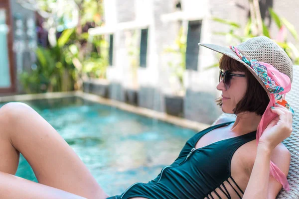 Schoonheid sexy vrouw met hoed en zonnebril haar zomervakantie genieten bij zwembad op een luxevilla. De zomervakantie is idyllisch. Tropische eiland Bali, Indonesië. — Stockfoto