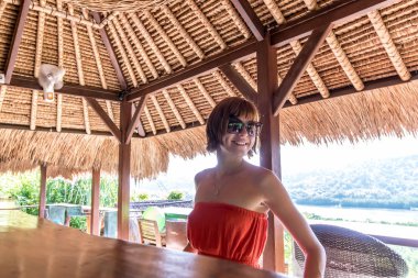 Tropikal bir kafede bir palmiye arka plan üzerinde Kırmızı elbiseli genç seksi kadın ağaçları ve tropik bitkiler. Bali, Endonezya.