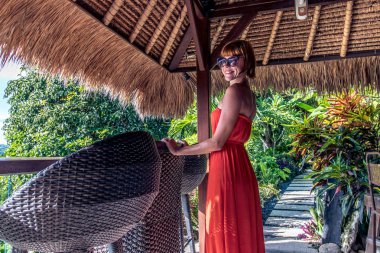 Tropikal bir kafede bir palmiye arka plan üzerinde Kırmızı elbiseli genç seksi kadın ağaçları ve tropik bitkiler. Bali, Endonezya.