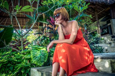 Bir tropik bahçe içinde Kırmızı elbiseli genç moda kadın. Mutlu kadın rahatlatıcı Bali Adası, Endonezya portresi.