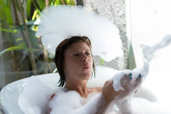 Junge Frau spielt mit Schaum in der Badewanne. tropisches Badezimmer in Luxusvilla, Bali Island, Indonesien. — Stockfoto