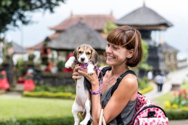 Kadın güzel genç haşhaş beagle köpek onun elinde tutan ile mutlu. Bali dili tapınak backgorund. Endonezya, Bali.