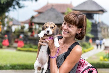 Kadın güzel genç haşhaş beagle köpek onun elinde tutan ile mutlu. Bali dili tapınak backgorund. Endonezya, Bali.