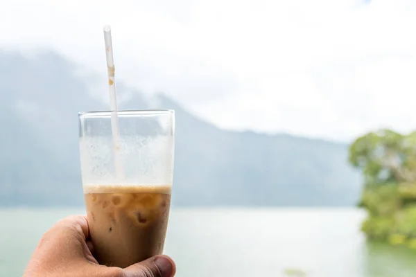 Mão de homem segurando café gelado ou café com café em um fundo de montanha. Ilha de Bali . — Fotografia de Stock