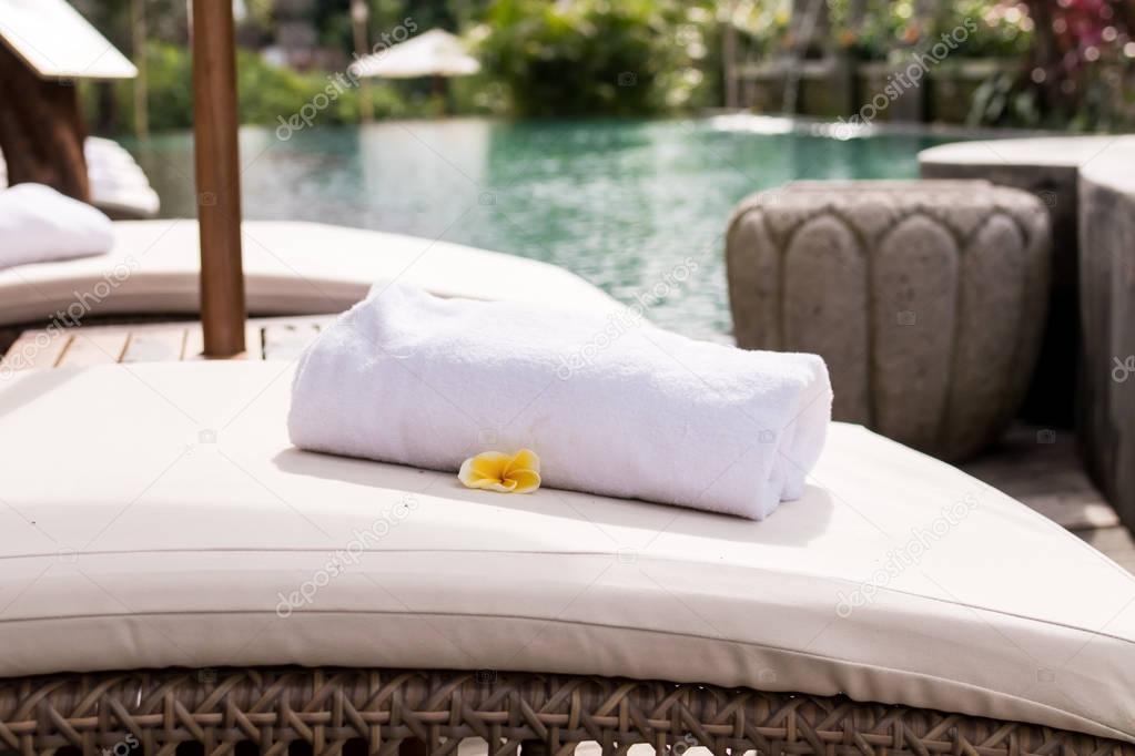 Close up of towel with plumeria frangipani on deck chair at resort pool. Bali island, Indonesia.