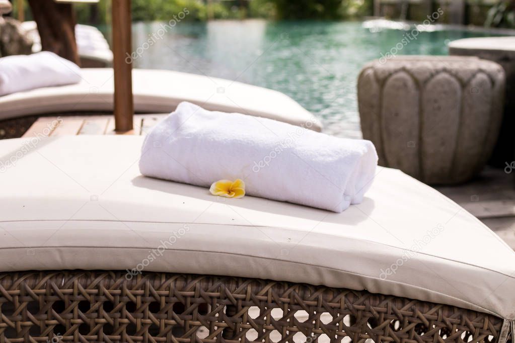 Close up of towel with plumeria frangipani on deck chair at resort pool. Bali island, Indonesia.