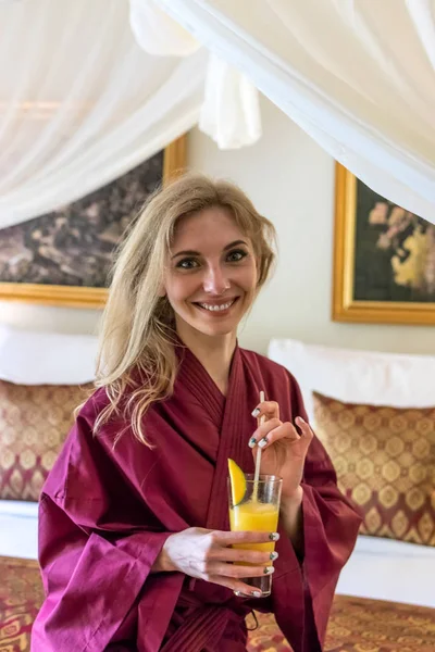 Portret vrij sexy meisje op bed in moderne appartement in de ochtend met mango sap. Bali eiland, villa. Vrouw in sexy badjas. — Stockfoto