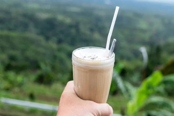 Gelo café latte em vidro mão homem em um belo fundo natureza. Ilha Tropical de Bali, Indonésia . — Fotografia de Stock
