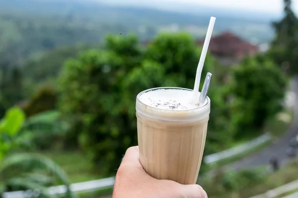 Ледяной кофе латте в руке человека стекла на красивом природном фоне. Тропический остров Бали . — стоковое фото