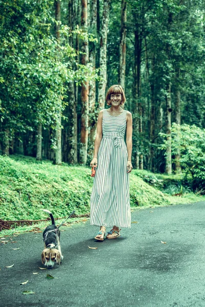 Mujer joven sosteniendo a su perro perrito beagle en la naturaleza de la isla tropical de Bali, Indonesia . —  Fotos de Stock