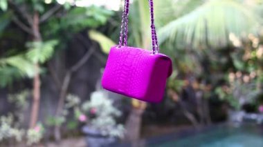 Moda lüks yılan derisi python çanta tropikal Bahçe arka plan üzerinde hareket. Bali Adası. Küçük pembe çanta.