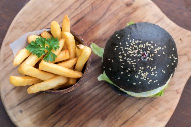 Siyah burger patty et, peynir, domates, mayonez, patates kızartması bir ahşap plaka ile. Modern hızlı yiyecek Öğle Yemeği.