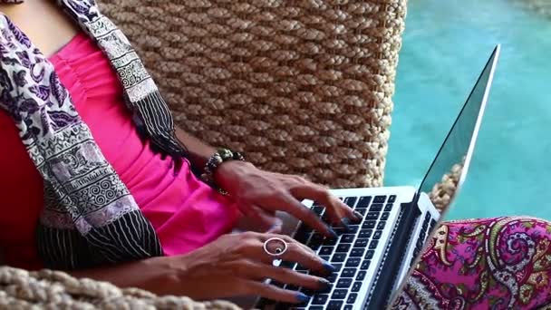 Женщина, работающая за ноутбуком, сидит в кресле у бассейна на острове Бали . — стоковое видео