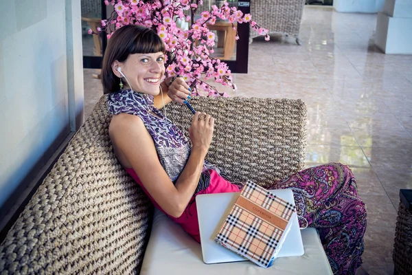 Beautiful young woman with notebook and laptop in the wooden coach outdoors, Bali island, villa.