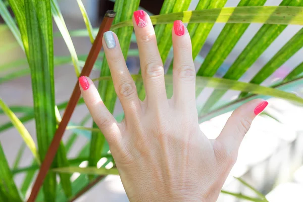Крупный план рук молодой женщины с красным маникюром на ногтях на естественном зеленом тропическом фоне . — стоковое фото